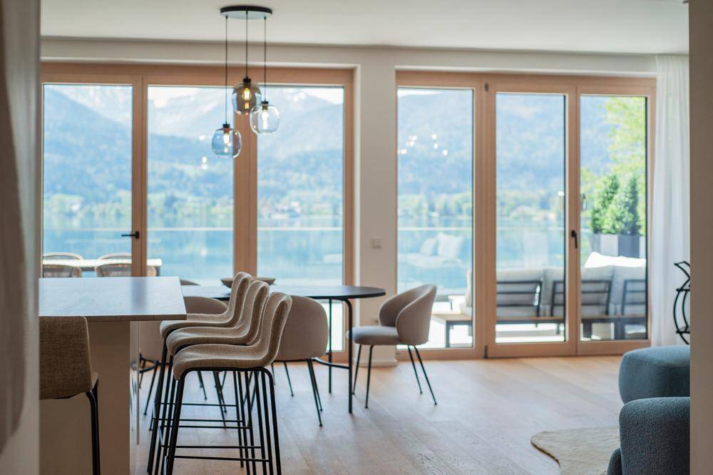 Moderner Essbereich mit Barhockern und Blick durch bodentiefe Fenster auf den See und die Berge.