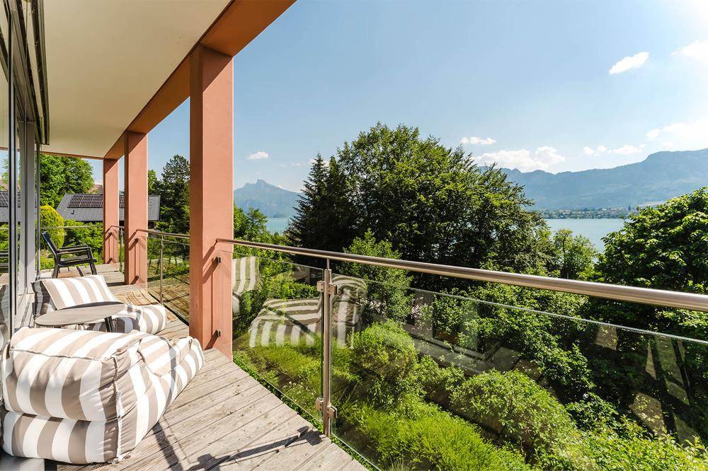 Geräumiger Balkon mit Glasgeländer und atemberaubendem Blick auf den See und die umliegende Natur.