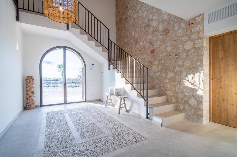 Heller Eingangsbereich mit Natursteinwand, eleganter Treppe und großem Bogenfenster.
