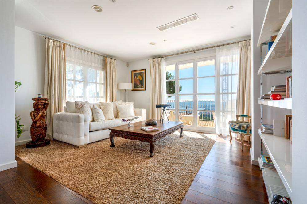 Gemütliches Wohnzimmer mit hellem Sofa, Teppichboden und Zugang zu einem Balkon mit Meerblick.