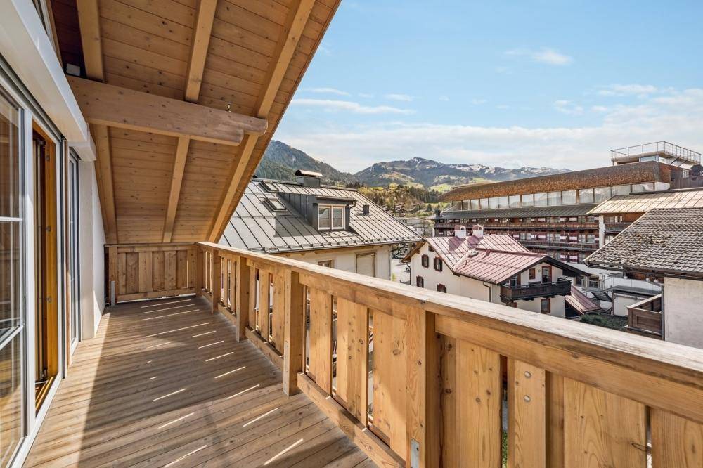 Großer Holzbalkon mit Bergblick und Aussicht auf die umliegenden Gebäude und Dächer.