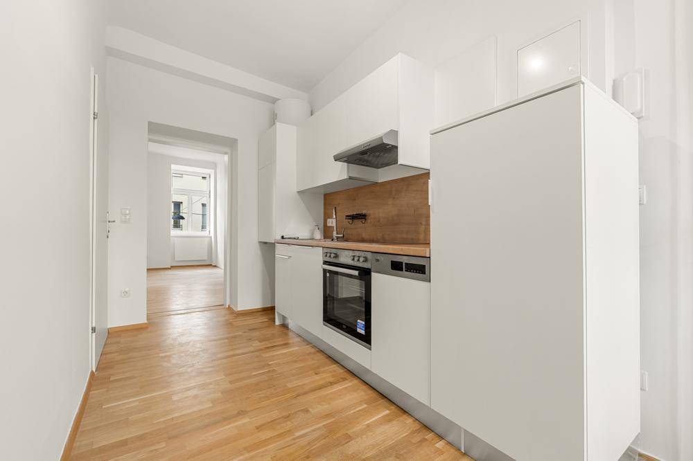 Moderne Einbauküche mit weißen Schränken, Holzdetails und integrierten Geräten in offenem Grundriss.