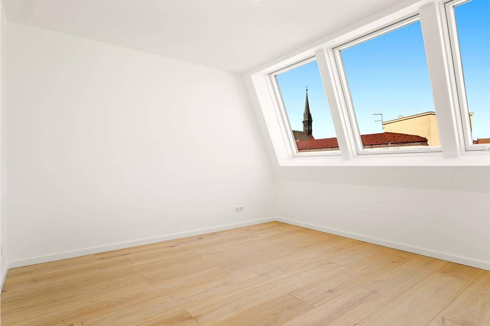 Gemütliches Schlafzimmer im Dachgeschoss mit Holzboden und Blick auf die Kirchturmspitze.