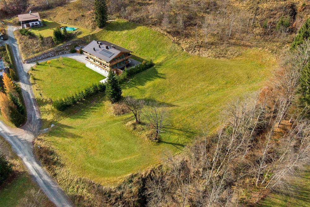 Luftaufnahme eines Hauses mit großem Grundstück, umgeben von grünen Wiesen und Bäumen in ländlicher Umgebung.