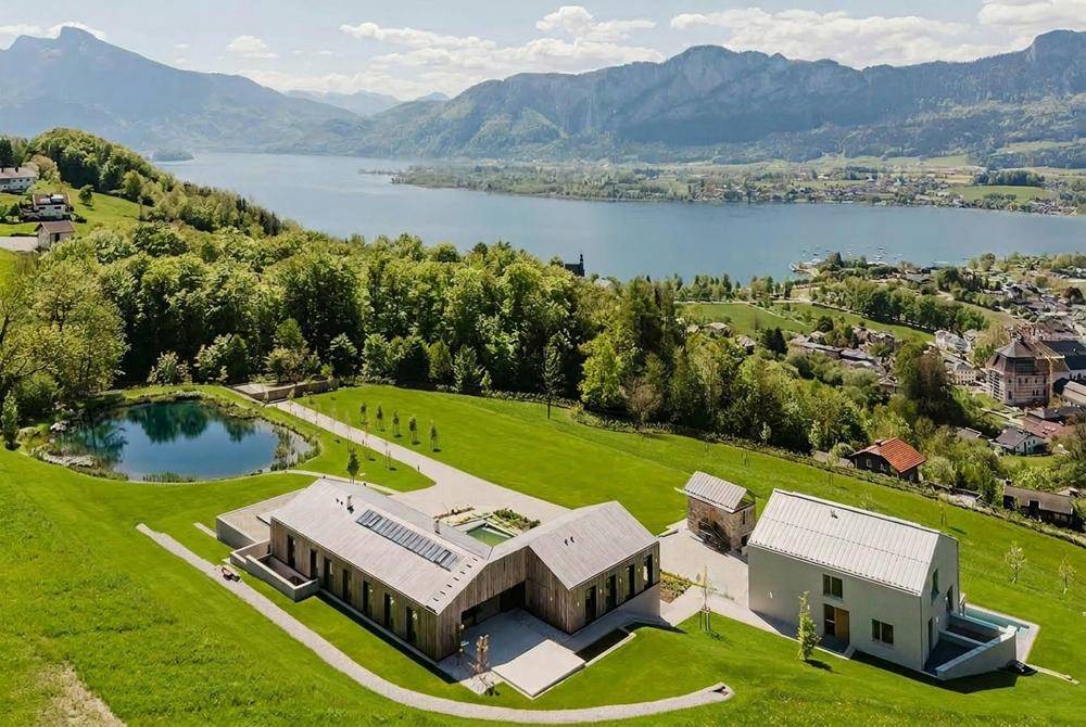 Weitläufiges Anwesen mit moderner Architektur, umgeben von Natur, See und Bergpanorama.