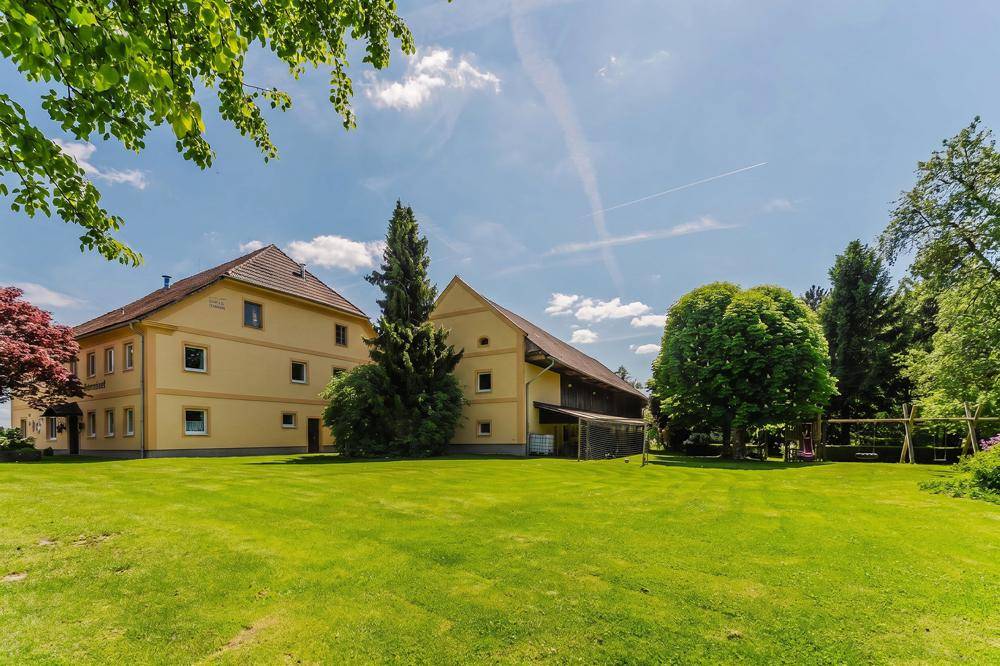 Weitläufige Rasenfläche vor dem historischen Gebäudeensemble mit altem Baumbestand und einem kleinen Spielplatz.