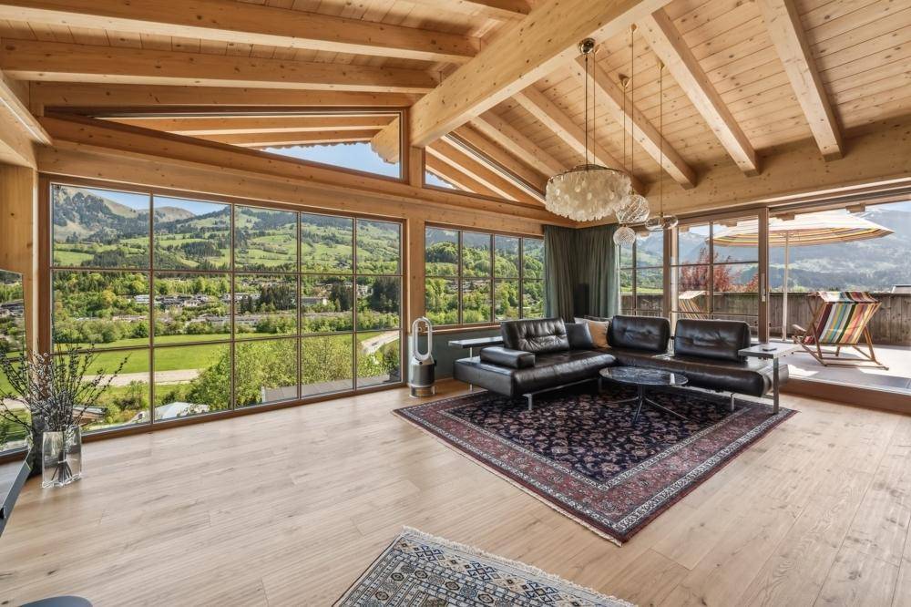 Lichtdurchflutetes Wohnzimmer mit Holzbalkendecke, großen Panoramafenstern und Bergblick.