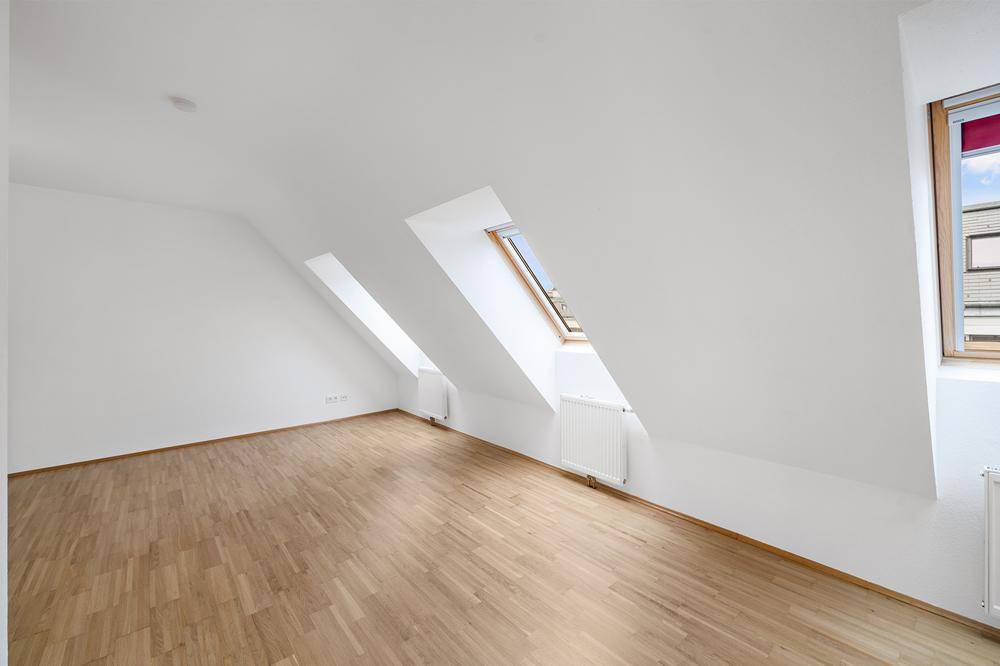 Ruhiges Zimmer im Dachgeschoss mit Holzboden und schrägen Wänden, ideal als Schlafzimmer.
