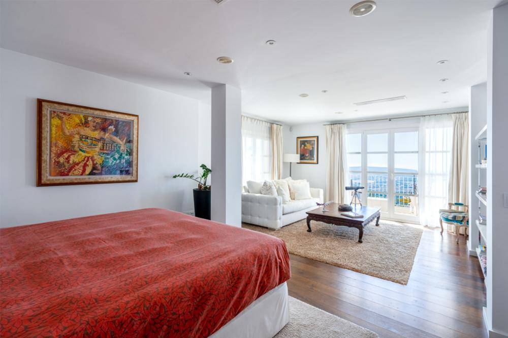 Geräumiges Schlafzimmer mit integriertem Wohnbereich und Zugang zu einem Balkon mit Meerblick.