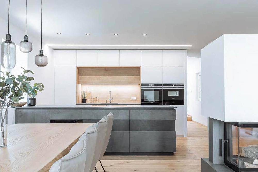 Moderne Küche mit weißen und grauen Fronten, Holzakzenten und integriertem Kamin.