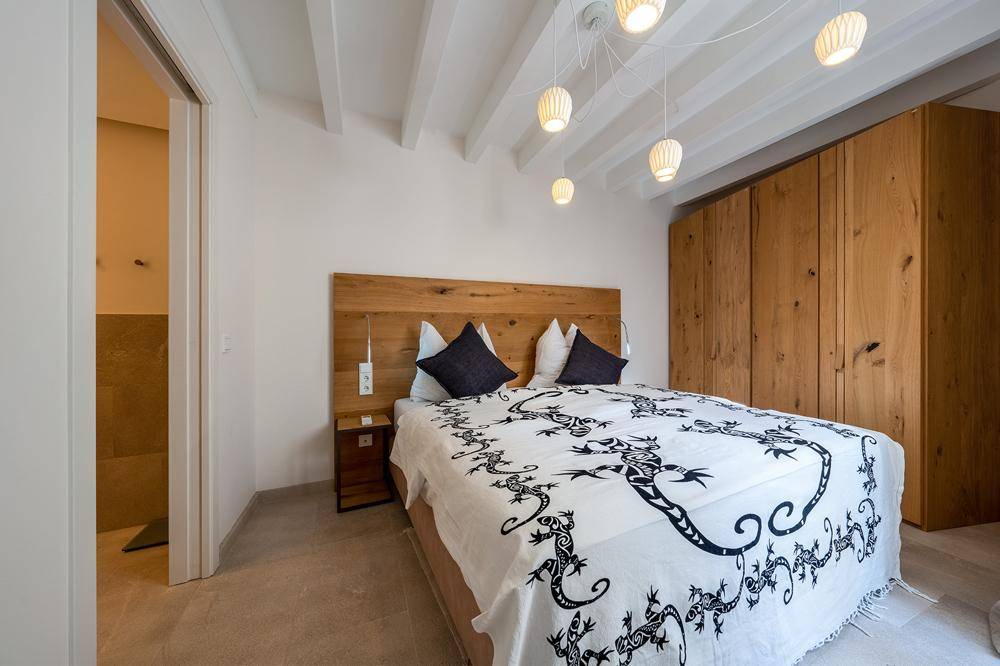 Schlafzimmer mit Holzbett, Einbauschränken und Deckenleuchten unter Holzbalkendecke.
