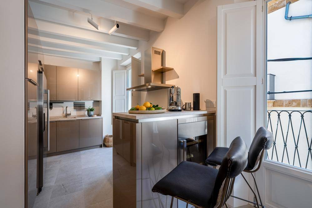Moderne Küche mit glänzenden Schränken, Kücheninsel und Zugang zu einem französischen Balkon.