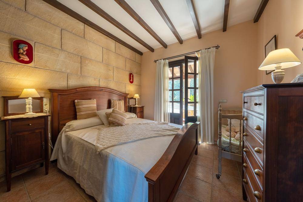 Gemütliches Schlafzimmer mit traditionellen Holzmöbeln, Steinwand und Zugang zu einem Außenbereich.