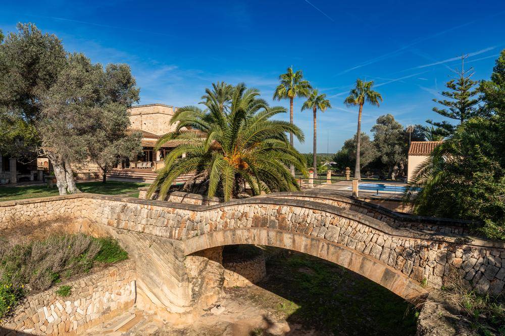Historische Steinbrücke auf dem weitläufigen Grundstück mit Blick auf das Haupthaus und den Poolbereich.