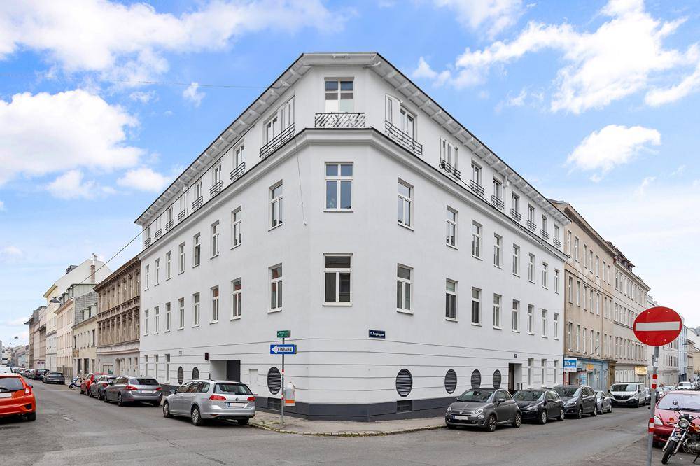 Weißes Eckgebäude mit moderner Architektur und vielen Fenstern an einer städtischen Straße.