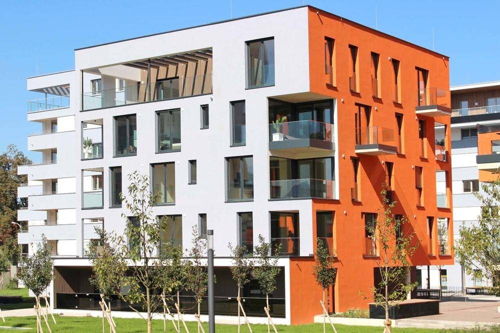 Modernes Wohngebäude mit auffälliger orangefarbener Fassade und großen Fensterfronten.