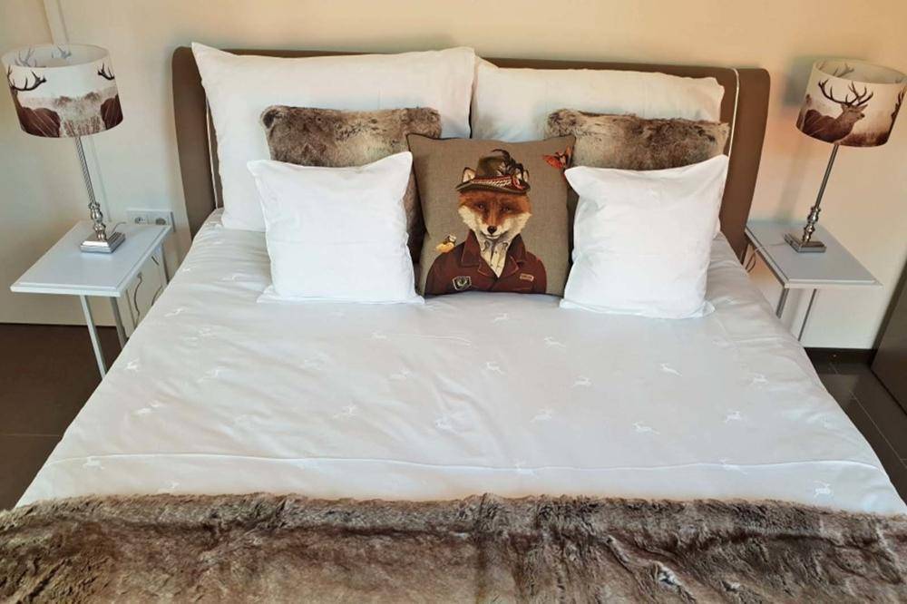 Komfortables Schlafzimmer mit Doppelbett, Hirschmotiv-Kissen und passenden Nachttischlampen.