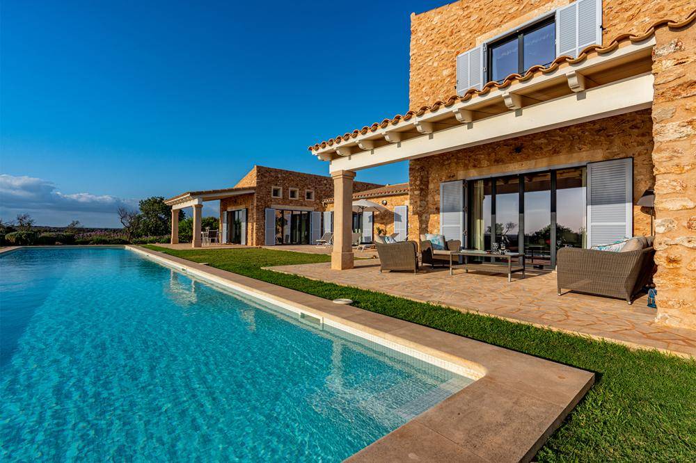 Sonniger Außenbereich der Villa mit großem Pool, Terrasse und mediterraner Architektur.