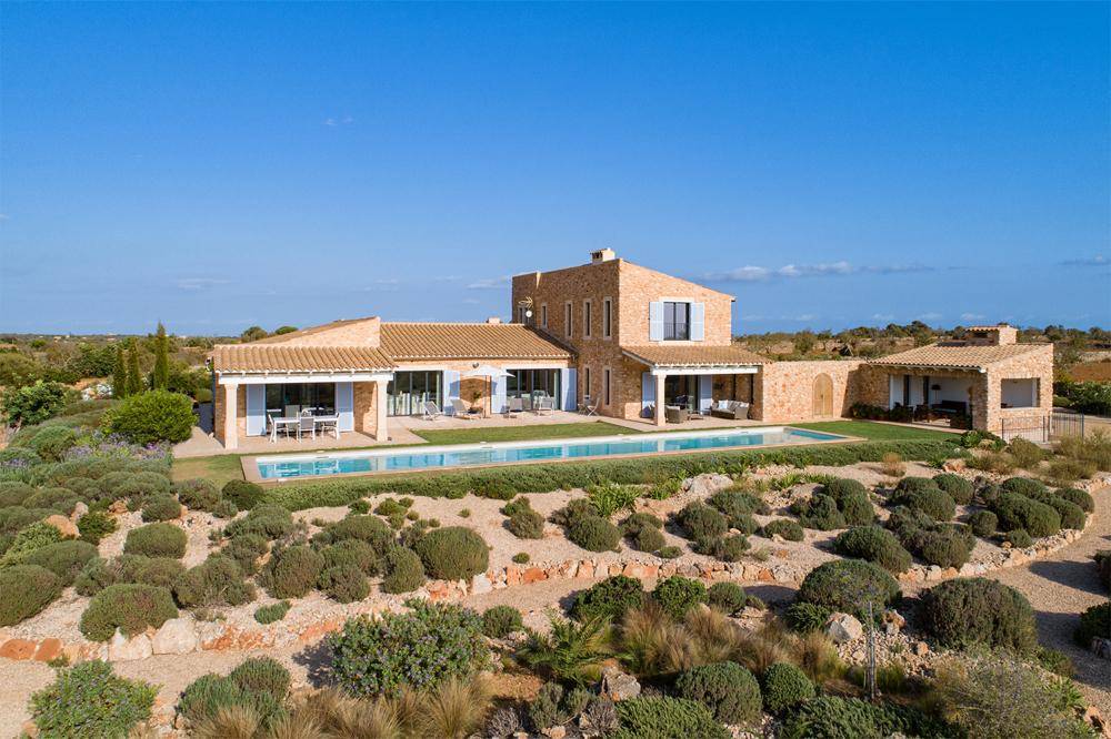 Weitläufige Villa mit großem Pool und mediterraner Gartenlandschaft unter blauem Himmel.
