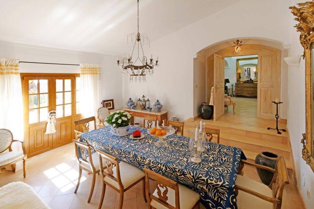 Elegantes Esszimmer mit großem Holztisch, Kronleuchter und einem Durchgang zu einem weiteren Raum.