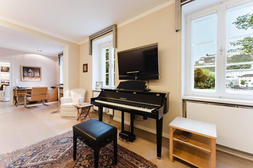 Geräumiger Wohnbereich mit Klavier, Fernseher und Blick auf die Umgebung durch große Fenster.