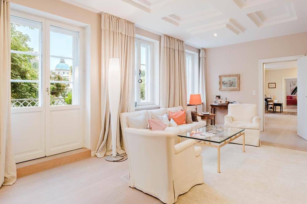 Helles Wohnzimmer mit eleganten Möbeln, Parkettboden und Zugang zu einem französischen Balkon.