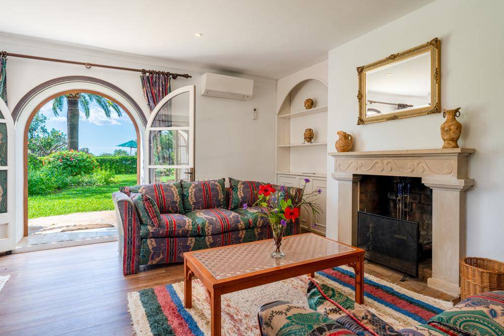Helles Wohnzimmer mit Kamin, Klimaanlage und Zugang zum Garten durch Rundbogenfenster.