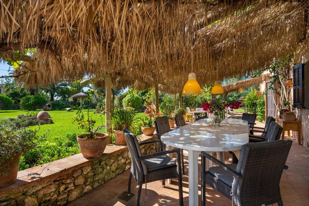 Überdachte Terrasse mit Strohdach, Esstisch und weitem Blick in den grünen Garten.