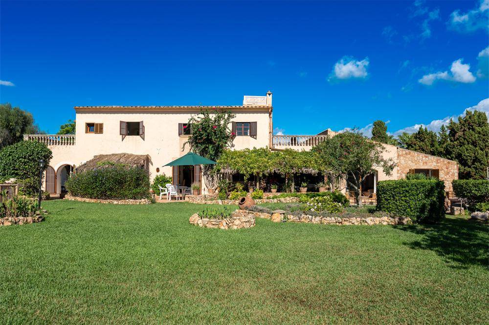 Weitläufiger Garten mit gepflegtem Rasen, mediterranen Pflanzen und einer überdachten Terrasse.
