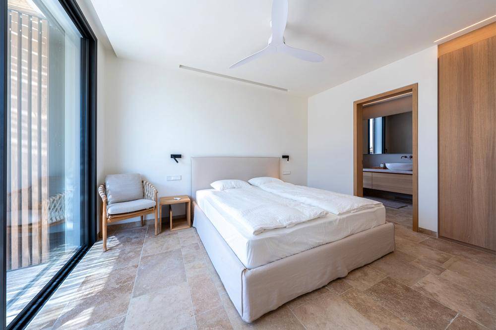 Helles Schlafzimmer mit Doppelbett, Fliesenboden und Zugang zu einem Balkon.