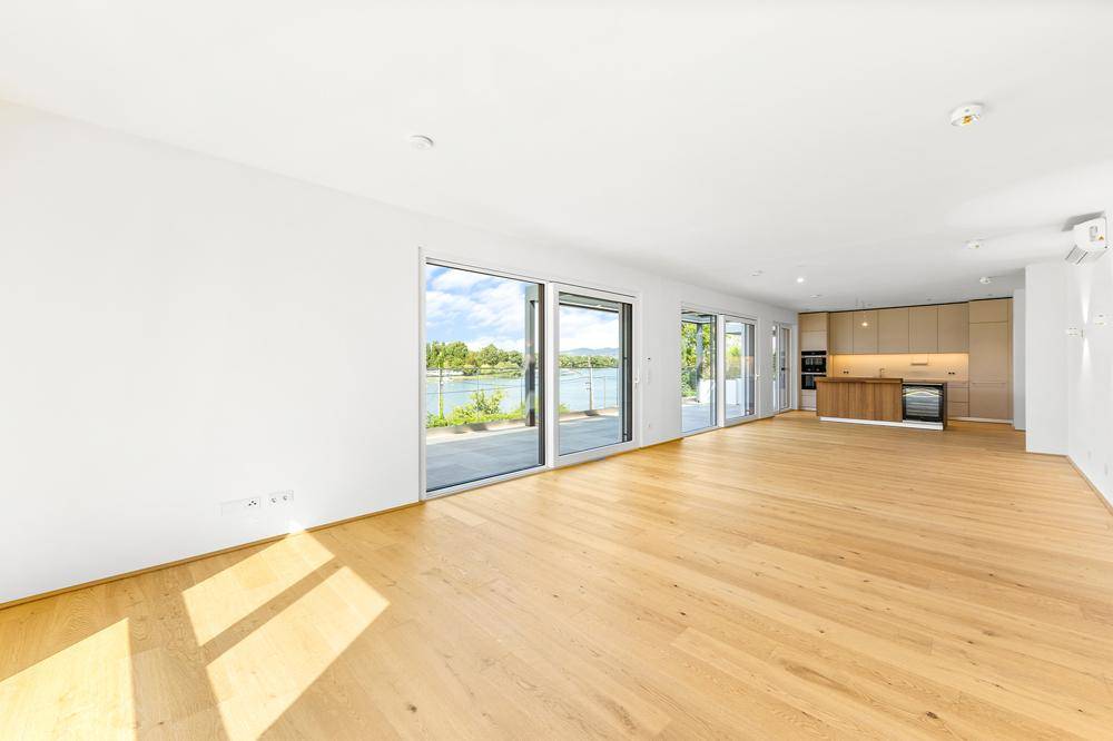 Heller, offener Wohnbereich mit Holzboden, großen Glasfronten und Blick auf das Wasser.