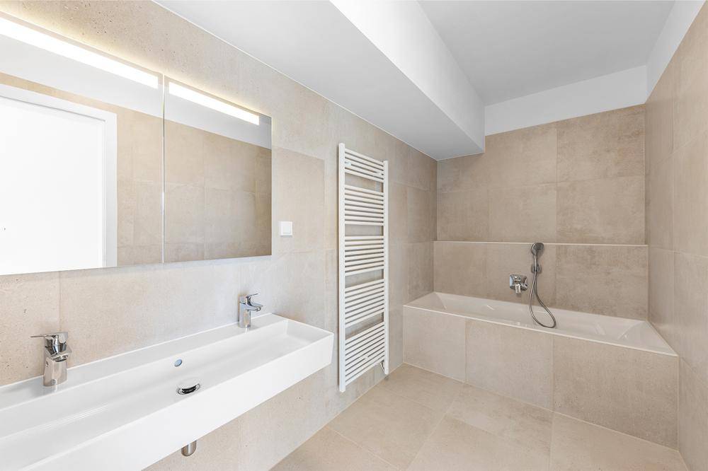 Modernes Badezimmer mit beigefarbenen Fliesen, Badewanne und Doppelwaschbecken.