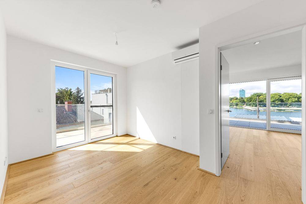 Helles Zimmer mit Holzboden, Klimaanlage und Zugang zu einem kleinen Balkon.