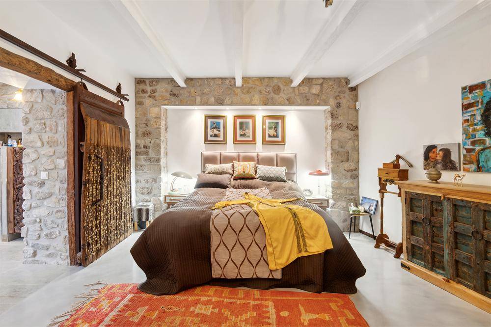 Gemütliches Schlafzimmer mit rustikalen Steinwänden, Holzbalken und einem komfortablen Bett in einer Nische.