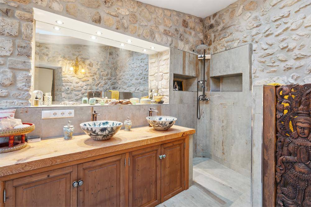 Rustikales Badezimmer mit Steinwänden, Doppelwaschbecken auf Holzplatte und einer begehbaren Dusche.