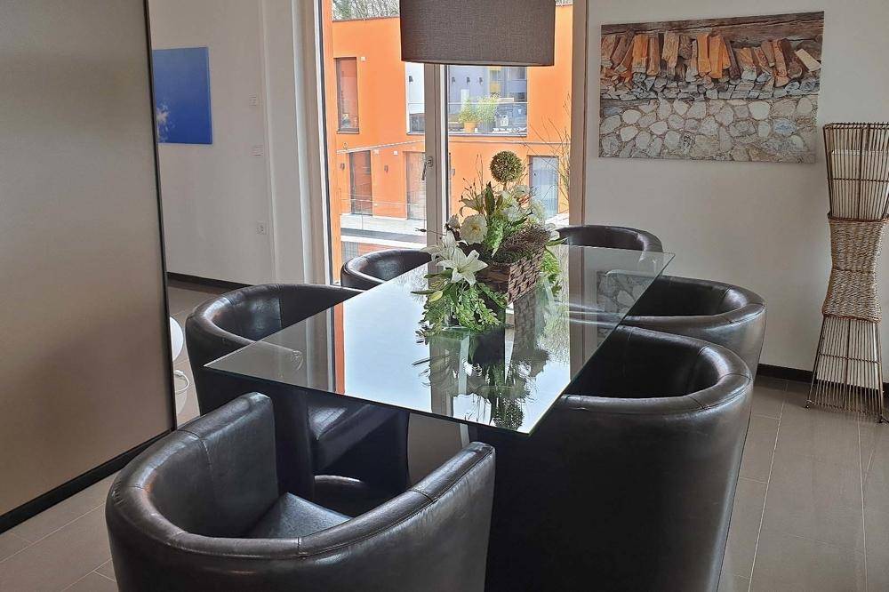 Eleganter Essbereich mit Glastisch und dunklen Ledersesseln, hell und modern eingerichtet.