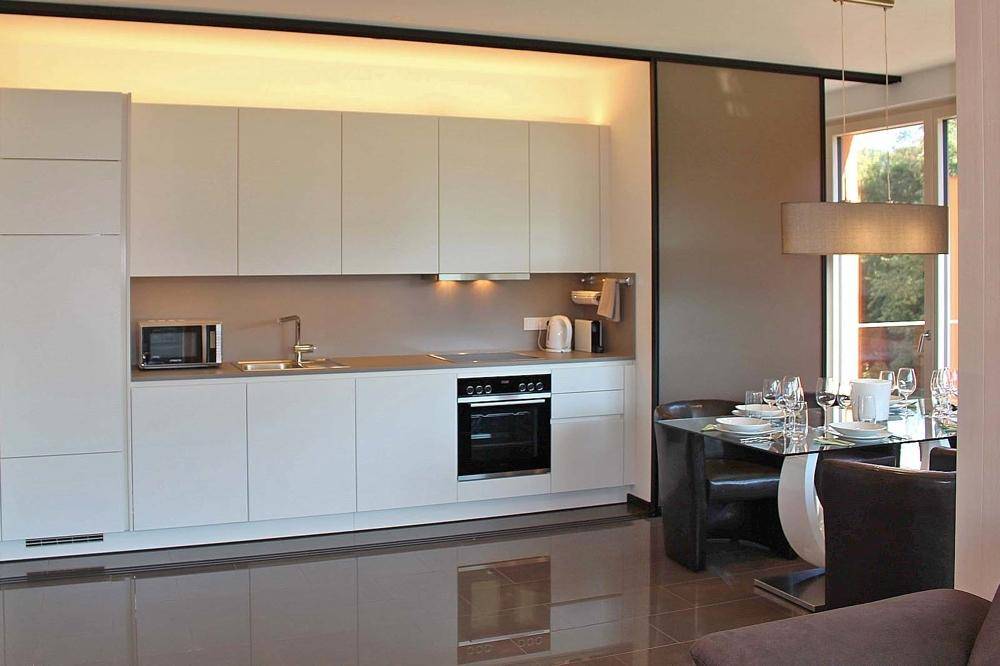 Moderne Einbauküche in hellem Design mit integrierten Geräten und Essbereich im Hintergrund.