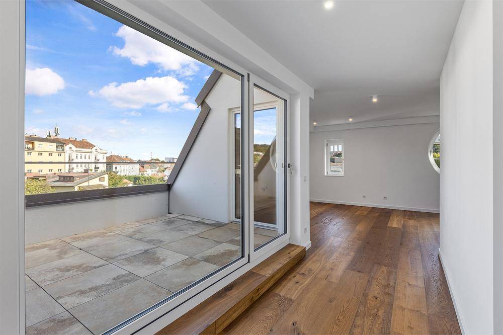 Lichtdurchfluteter Innenraum mit Holzboden und breitem Schiebetürzugang zu einer Dachterrasse mit Stadtblick.