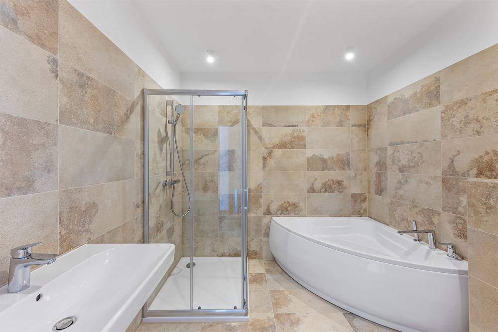 Modernes Badezimmer mit beigefarbenen Fliesen, Duschkabine und einer eleganten Eckbadewanne.