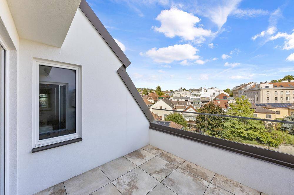 Moderne Dachterrasse mit Fliesenboden, Glasgeländer und weitem Blick über die Stadt.