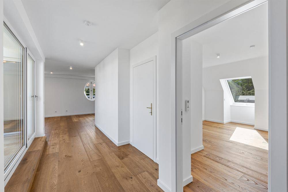 Heller Flur mit Holzboden, der verschiedene Bereiche verbindet, mit einem runden Fenster und Oberlicht.
