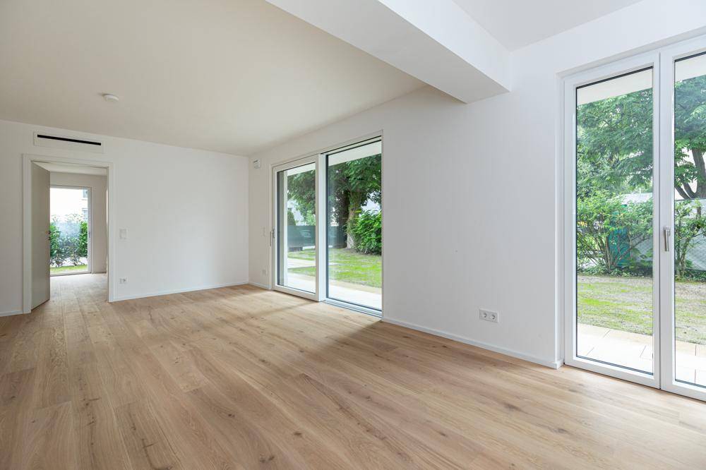 Heller, leerer Wohnraum mit Eichenparkett und großen Schiebetüren zum Garten.