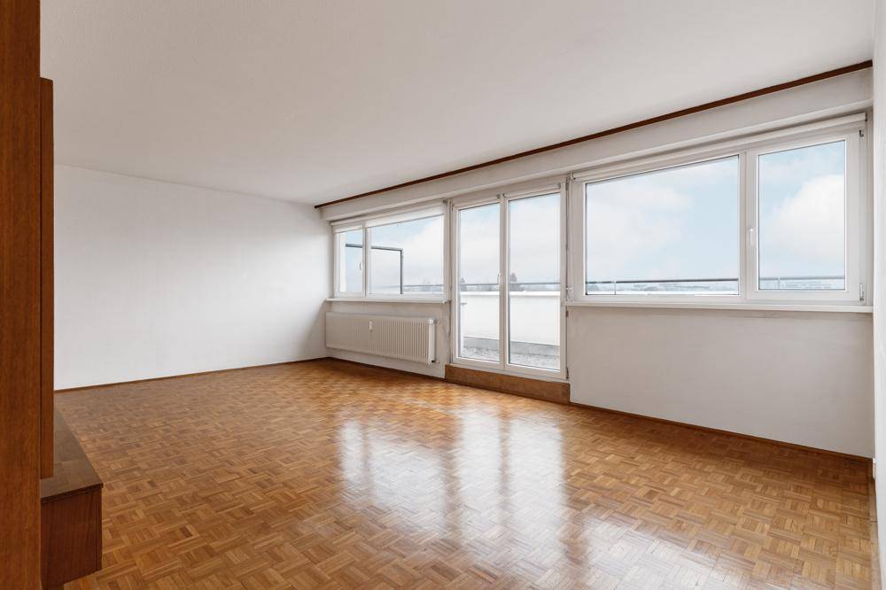 Helles Wohnzimmer mit Fischgrätparkettboden und Zugang zu einem Balkon oder einer Terrasse.