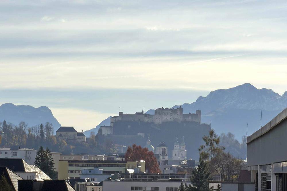 Panoramablick über eine historische Stadt mit Burg und majestätischen Bergen im Hintergrund.