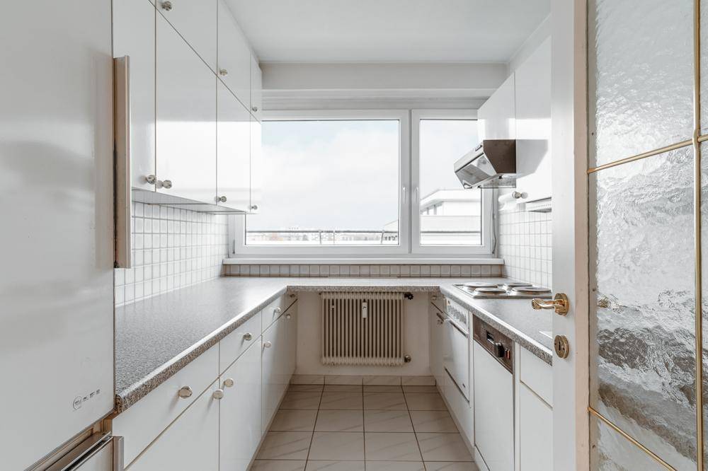 Kleine, funktionale Küche mit weißen Schränken, Fliesenboden und einem Fenster.