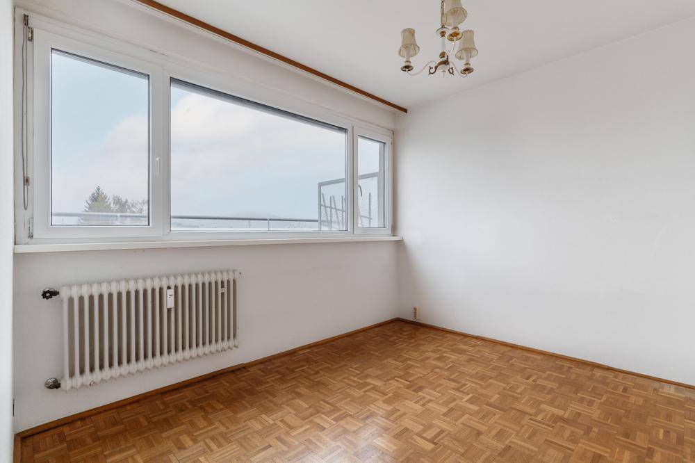 Leeres Schlafzimmer mit Parkettboden und großem Fenster, das viel Tageslicht hereinlässt.