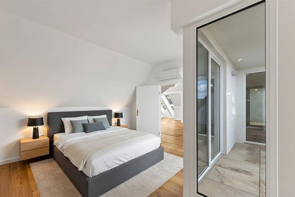 Schlafzimmer mit Doppelbett, Holzboden und Zugang zu einem hellen Balkon mit Ausblick.