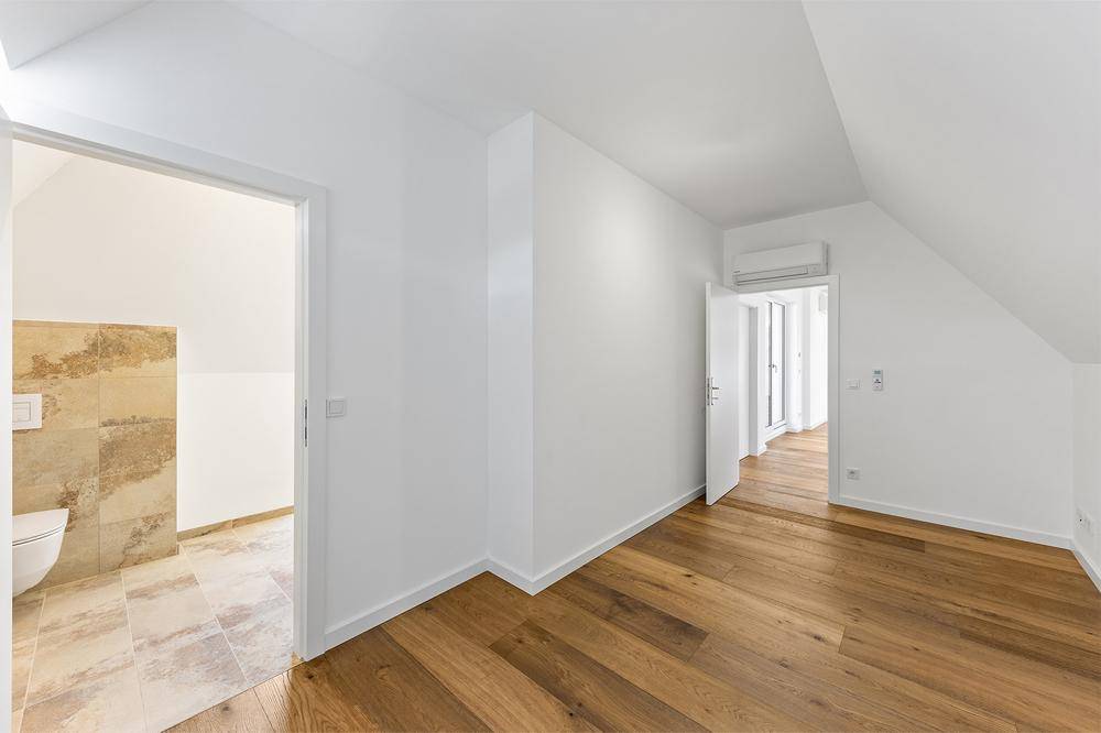 Heller Raum mit Holzboden und Zugang zu einem Badezimmer, unter einer Dachschräge gelegen.