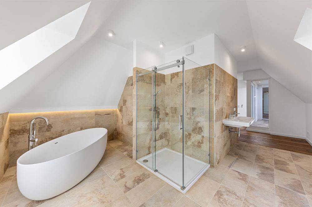 Modernes Badezimmer mit freistehender Badewanne, begehbarer Dusche und hellen Fliesen unter Dachschrägen.