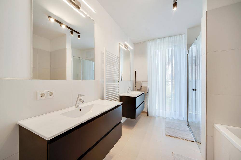 Modernes Badezimmer mit Doppelwaschbecken, großer Dusche und Fenster mit weißem Vorhang.